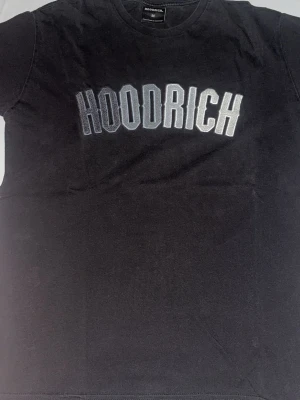 Svart HOODRICH t-shirt - Säljer en svart t-shirt från HOODRICH i storlek M. T-shirten har ett stort broderat HOODRICH-tryck i vitt och grått på bröstet. Klassisk rund hals och korta ärmar. Perfekt för dig som gillar streetwear och vill sticka ut.