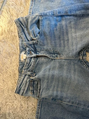 Ljusblå raka jeans med strass - Säljer ett par ljusblå jeans med raka ben och hög midja. Jeansen har coola strassdetaljer på benen och klassisk femficksmodell. Tillverkade i denim med dragkedjegylf och bälteshällor. Perfekta för dig som vill sticka ut lite extra!