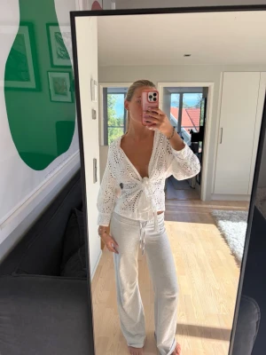 Vit spetsblus med knyt och broderi - Säljer en superfin vit blus i spets med broderade detaljer och knyt framtill. Blusen har v-ringning, långa ärmar och är lätt genomskinlig. Perfekt att styla med jeans eller kjol för en trendig look.