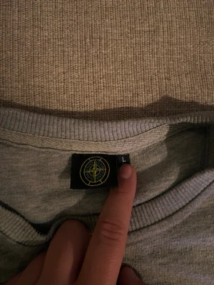 Grå sweatshirt från Stone Island - Snygg grå sweatshirt från Stone Island med klassisk logga på bröstet och ärmen. Tröjan har rund halsringning, ribbade muddar vid ärmslut och nederkant samt en avslappnad passform. Perfekt för en casual och trendig look.