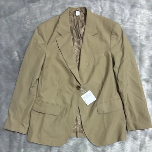 Beige Blazer från Carin Wester, storlek 38 - Stilren beige kavaj från Carin Wester i storlek 38. Klassisk modell med två framfickor med lock, bröstficka och ett knappslå framtill. Fodrad insida i matchande ton. Perfekt för en dressad look och enkel att matcha med olika outfits. Inköpt för 899kr