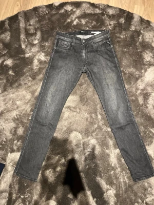 Grå slim fit jeans från Replay - Snygga grå slim fit jeans från Replay med klassisk femficksdesign och diskreta slitningar framtill. Jeansen har normal midja och smala ben, perfekta för en trendig och avslappnad stil. Tillverkade i stretchigt denim för extra komfort. 30/31