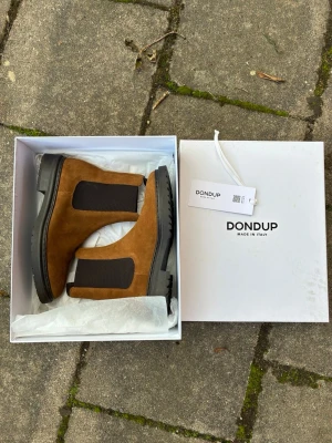 Bruna Chelsea boots från Dondup - Snygga Chelsea boots i mocka från Dondup. Skorna är bruna med breda svarta resårpaneler på sidorna och har en robust svart sula. Klassisk siluett med dragflik bak för enkel påtagning. Perfekta för dig som vill ha stilrena boots med modern touch.