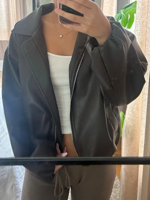 Svart oversized skinnjacka - Säljer en svart oversized skinnjacka med dragkedja framtill och bred krage. Jackan har en avslappnad passform och är perfekt för dig som vill ha en cool och enkel look. Passar till det mesta och är lätt att styla.