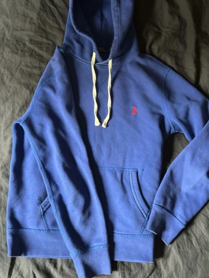 Blå hoodie från Polo Ralph Lauren  - Snygg blå hoodie från Polo Ralph Lauren med vit dragsko och klassisk röd logga broderad på bröstet. Hoodien har känguruficka framtill. Säljs då den är för liten, kom gärna med prisförslag eller byten☺️