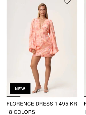 Kort rosa omlottklänning med knappar - Trendig kort klänning i rosa och ljusa toner med omlottdesign och knappar framtill. Klänningen har djup v-ringning och långa puffärmar som ger en cool och modern look. Perfekt för dig som vill sticka ut med en färgstark och unik stil.