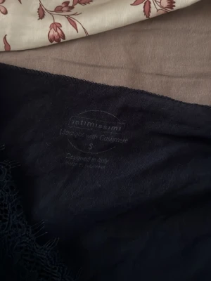 Mörkblå långärmad topp från Intimissimi - Säljer en mörkblå långärmad topp från Intimissimi med spetsdetalj vid v-ringningen och ärmsluten. Toppen är i mjuk bomull och har en slim passform som sitter snyggt på kroppen. Helt oanvänd.