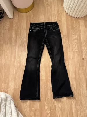 Svarta bootcut jeans med vita sömmar - Säljer ett par svarta bootcut jeans med markerade vita sömmar och broderade bakfickor. Jeansen har klassisk femficksdesign och utsvängda ben. Perfekta för dig som vill ha en retro och trendig look.