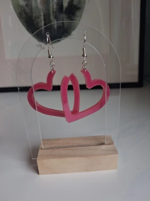 Rosa hjärtformade örhängen resin/epoxy handgjorda - Säljer ett par coola örhängen i form av öppna hjärtan i skapade i resin/epoxy. Öronkroken är nickelsäker. Längd ca 4.5cm långa. Perfekta för dig som vill addera lite färg och personlighet till din stil.