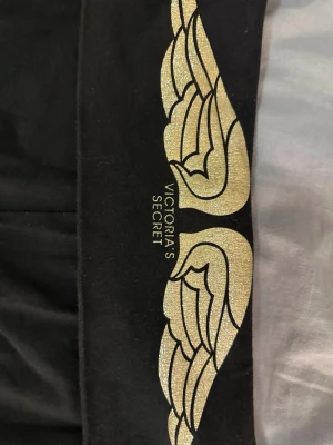 Vintage  Victoria's Secret jogging pants  - Snygga svarta leggings från Victoria's Secret med guldiga änglavingar och logga på midjebandet. Stretchigt material och utsvängda ben ger en bekväm och trendig look. Perfekta för dig som vill ha något extra till din outfit. Storlek short M                                                                       Pris går att diskutera, hör av dig för fler frågor 🌷 00s #vintage 