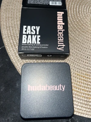 Huda Beauty Easy Bake Cherry Blossom - Loose baking & setting powder från Huda Beauty i nyansen Cherry Blossom Cake. Kommer i en stilren svart fyrkantig burk med rosa detaljer och tillhörande kartong. Perfekt för att fixera sminket och ge en matt finish. Innehåller 20 g.