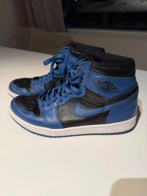 Nike sneakers - Snygga höga sneakers från Nike i blått och svart med vit sula. Skorna har klassisk snörning, vadderad krage och ikonisk logga på sidan. Tillverkade i läder med perforerad tåbox för extra ventilation. Perfekta för dig som gillar streetwear och sportig stil.