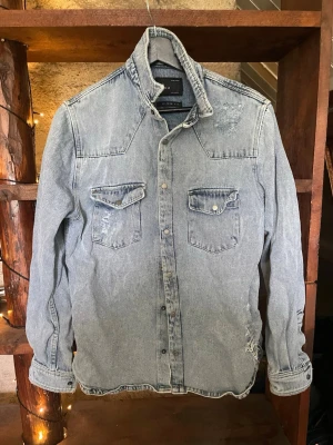 Ljusblå jeansjacka från Zara Man - Säljer en ljusblå jeansjacka från Zara Man i relaxed fit. Jackan har två bröstfickor med lock och knapp, slitna detaljer och klassisk krage. Perfekt för en avslappnad och trendig look.