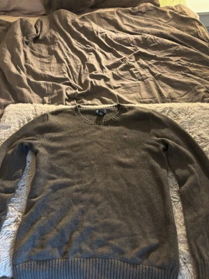 Grå stickad tröja från Polo Ralph Lauren - Mysig grå stickad tröja från Polo Ralph Lauren med rund halsringning och diskret broderad logga på bröstet. Tillverkad i mjuk bomull som passar perfekt för kyliga dagar. Klassisk och enkel design som funkar till det mesta.