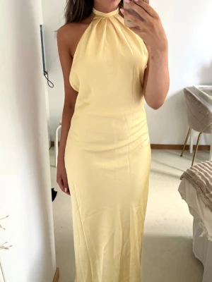 Ljusgul balklänning med halterneck i satin - Ny, oanvänd maxiklänning från Indefeir Studios med tags kvar. Elegant halterneckmodell med öppen rygg och ett vackert satinliknande tyg i en mjuk smörgulfärgad nyans. Perfekt till bröllop, student, bal, sittningar, midsommar, semester eller andra festliga tillfällen. Halterneck med knytning i nacken. Maxilängd💓