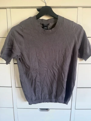 Grå kortärmad topp från Lindex - En enkel och stilren grå topp från Lindex i storlek XS. Toppen har rund halsringning, korta ärmar och är tillverkad i ett mjukt material som känns bekvämt mot huden. Perfekt att matcha med jeans eller kjol för en clean look.