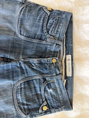 GAP jeans  - Snygga blå jeans från GAP med slitna detaljer och kontrastsömmar. Jeansen är lågmidjade och boot cut