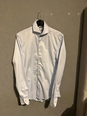 Klassisk vit skjorta med knappar - Säljer en stilren vit skjorta med långa ärmar och klassisk krage. Skjortan har knappar framtill och vid ärmsluten. Perfekt för dig som gillar en clean och enkel look. Tillverkad i bomull för en bekväm känsla.