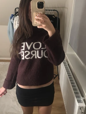 Brun stickad tröja med text - Mysig brun stickad tröja med polokrage och vit text 'LOVE YOURSELF' framtill. Tröjan har långa ärmar och ribbade muddar vid ärmslut och nederkant. Perfekt för dig som gillar statement-plagg och vill ha något bekvämt och trendigt.