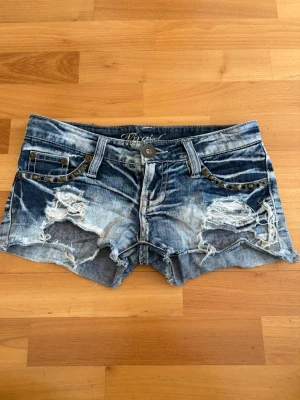 Blå slitna jeansshorts med nitar - Passar ca w25🥰🥰Säljer ett par blå jeansshorts med slitna detaljer och råa kanter. Shortsen har nitar vid fickorna framtill och klassisk femficksdesign. Perfekta för en avslappnad och edgy stil.