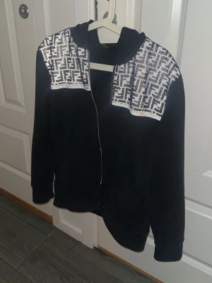 Fendi hoodie MONOGRAM   - Fendi kofta köpt på Kaspersheat för 3500kr. STORLEK XS. På axlarna finns stora glittriga partier med ett grafiskt mönster i vitt och silver som ger en riktigt unik look. Hoodien har långa ärmar och är perfekt för dig som vill sticka ut lite extra.