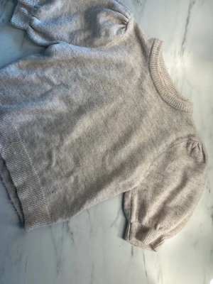 Beige stickad topp från Gina Tricot - Säljer en ljusbeige stickad topp från Gina Tricot med kort puffärm och ribbade muddar. 