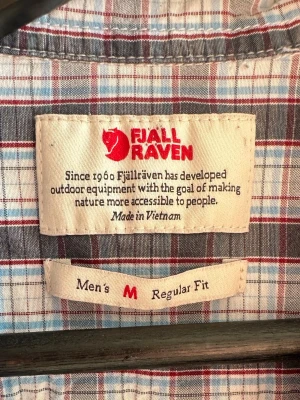 Rutig kortärmad skjorta Fjällräven - Säljer denna vintage abisko cool tröjan från fjällreäven, som inte lägre säljs i denhär färgen! Kortärmad rutig design med blå, röda och vita/ grå toner. Skjortan har två bröstfickor med knappar och klassisk krage. Regular fit strlk M.Materialet består av 100% Tencel Lyocell. 