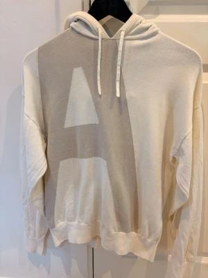  Armani exchange hoodie  - Snygg vit hoodie med stora grafiska bokstäver i beige och grått på både fram- och baksida. Hoodien har dragsko i huvan och ribbade muddar vid ärmar och nederkant. Perfekt för en avslappnad och trendig stil.