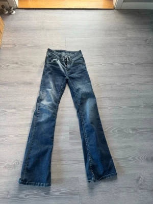 Blå bootcut jeans low waist XS L32 - Säljer ett par blå bootcut jeans med låg midja. Jeansen har klassisk femficksdesign, dubbla knappar i midjan och snygg tvättad look. Perfekta för dig som gillar en avslappnad men ändå trendig stil.