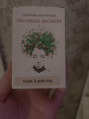 Handgjord olivtvål musk & rosa lera - Handgjord olivoljetvål från Electra's Secrets med doft av musk och rosa lera. Tvålen är ljusrosa och kommer i en vit förpackning med konstnärlig design. Perfekt för dig som vill ha en naturlig och lyxig tvål till din hudvårdsrutin.