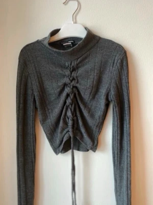 Grå ribbad croppad topp med snörning - Super fin långärmad topp från Fashionnova, har tyvärr inte kvar storlekslappen då den kliade, men är helt säker på att tröjan är i storlek S 🥹