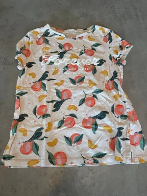 Vit t-shirt med fruktmönster från H&M - Säljer en vit t-shirt från H&M med färgglatt fruktmönster i orange, gul och grönt. Trycket på bröstet säger 'Dreamer Forever'. T-shirten har korta ärmar och är gjord i mjuk bomull, perfekt för en chill och färgglad stil.