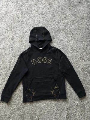 Svart hoodie från BOSS med guldtryck - En riktigt snygg hugo boss tröja, använd max 10 gånger fick den av min vän som som present den är riktigt snygg och passar till allt bara lite vid trycket de gått av men man märker inte när man har den på sig. Inga report eller solbränna på själva tröjan. Den är princip helt ny