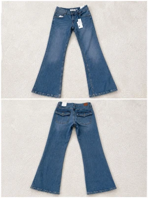 Blå bootcut jeans med rå kant - Säljer ett par ljusblå bootcut jeans med rå, fransad kant nertill. Jeansen har klassiska bakfickor med dekorativa sömmar och normal midja. Tillverkade i denim med en avslappnad passform som ger en cool retrovibe. Jeasen är oanvända.  