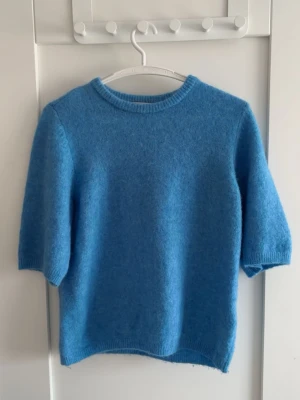 Blå stickad tröja med halvlånga ärmar - Blå stickad tröja med rund halsringning och halvlånga ärmar. Tröjan är gjord på alpacka, bomull och polyester. Den är i jättebra skick och är endast använd en gång