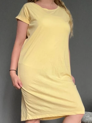 Ljusgul enkel t-shirtklänning - En basic ljusgul t-shirtklänning med rund hals och korta ärmar. Klänningen har rak passform. Stilren och enkel design utan mönster eller detaljer. I fint skick. Tunt tyg så det kan vara lite genomskinligt.
