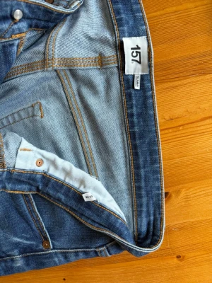 Blå slim fit jeans från 157 - Säljer ett par klassiska blå slim fit jeans från 157. Jeansen har normal midja, smala ben och snygga slitningar framtill. Tillverkade i denim med kontrastsömmar och femficksmodell. Perfekta för en trendig och avslappnad stil.