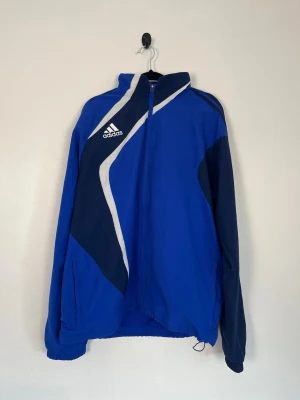 Adidas Track Jacket Blå Marinblå XL Träningsjacka Zip Jacket Retro Y2K - • Storlek: XL • Färg: Blå, marinblå, vit och svart • Passform: Regular Fit  • Krage: Hög ståkrage • Material: Yttertyg 100 % polyester, Foder 100 % polyester (mesh)  Skick: Plagget är i väldigt fint skick. Eventuella anmärkningar anges alltid tydligt i beskrivningen och visas på bilderna.  Nypris: Cirka 900 kr.  📦 Skickas snabbt och packas omsorgsfullt. 💬 Hör gärna av dig om du har frågor eller vill se fler bilder. 🤝 Samfrakt erbjuds vid köp av flera plagg – kika gärna in mina andra annonser!
