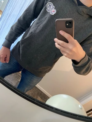 Mörkgrå hoodie med tryck - Snygg mörkgrå hoodie med huva och ett litet vitt och rött tryck på bröstet. Hoodien har ribbade muddar vid ärmslut och nederkant samt en klassisk passform. Perfekt för en avslappnad och trendig stil. OBS!Storlek M men passar S också!