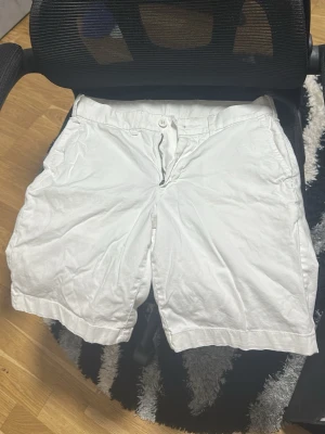 Vita klassiska shorts med fickor - Säljer ett par vita shorts med normal passform och praktiska sidofickor. De har knapp och dragkedja framtill samt bakfickor med knapp. Perfekta för sommaren och enkla att matcha med olika stilar.