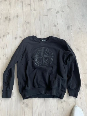 Stone Island  - Svart sweatshirt med stor Stone Island-logga i svart på bröstet. Tröjan har rund halsringning, långa ärmar och ribbade muddar vid ärmslut och nederkant. Perfekt för en avslappnad och stilren look. Riktigt fin, använda max en eller två gånger. OBS! Siri loggan följer ej med därav priset. Står 3xl men skulle säga att det är m/l