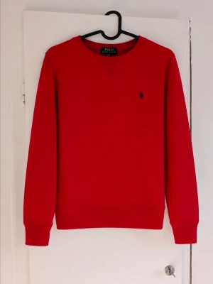 Ralph Lauren sweatshirt - Säljer en klassisk sweatshirt från Polo Ralph Lauren i en snygg röd färg med broderad logga på bröstet. Perfekt för både vardag och en mer uppklädd, avslappnad stil. Mjuk och bekväm passform som passar året runt. • Märke: Polo Ralph Lauren • Färg: Röd • Storlek: L (14-16) • Skick: Mycket fint skick, sparsamt använd men har en fläck och den är lite nopprig! • Detaljer: Broderad logga på bröstet och ribbade muddar