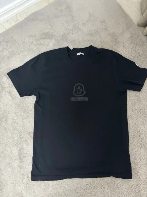 Moncler t shirt med logo i mitten  - Svart Moncler t shirt med logo på mitten av t shirten och på armen med en rund logo  inte används har bara liggit u mot garderob kan gå ner med pris om behövs