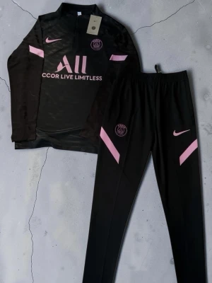 Svart PSG träningsset med rosa detaljer - .🔥⚽ PSG Träningsset ⚽🔥  🖤svart och rosa PSG-set 👕 Långärmad träningströja med dragkedja 👖 Matchande träningsbyxor 🧸 Mjukt & bekvämt material 💪 Perfekt för träning, fotboll och vardag ✨ Snygg PSG-design med detaljer som sticker ut 😎 Sportig & clean fit 🏃‍♂️ Skönt set att bära både på planen och till vardags  📏 Storlek: (M) 💯 Skick: Nytt 💸 Pris: (600kr)  📩 DM vid intresse eller frågor 🚨 Först till kvarn gäller! 🔥  #PSG #ParisSaintGermain #Fotboll #Träningsset #Fotbollskläder
