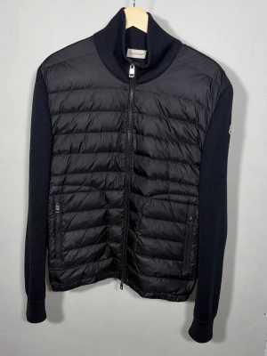 Maglione Tricot Cardigan - Svart hybridjacka från Moncler. Extremt eftertraktad och populär modell. Jackan är i riktigt fint skick och har endast en ytterst liten flaw på en av ärmsluten, se bild 6. Storlek L, sitter mer som en Medium då Moncler är något små i storlekarna.