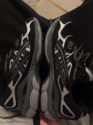 Svarta och grå sneakers med meshdetaljer - Snygga sneakers i svart och grått med vita detaljer och meshpaneler för extra ventilation. Skorna har en sportig look med robust sula och klassisk snörning. Perfekta för dig som gillar streetwear och sportig stil.