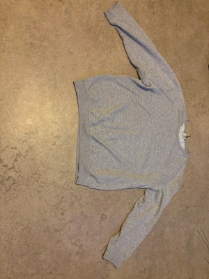 Ljusgrå sweater - En enkel och stilren ljusgrå sweater med klassisk känguruficka framtill och långa ärmar. Sweatern har ribbade muddar vid ärmslut och nederkant. Perfekt för en avslappnad look.