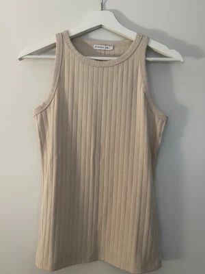 Beige ribbad linnetopp från Stockh lm - Snygg beige ribbad linnetopp från Stockh lm. Toppen är ärmlös med rund halsringning och har en tight passform. Perfekt att styla med jeans eller kjol för en clean och enkel look.