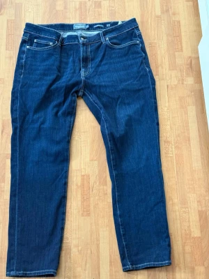 Mörkblå raka jeans herr - Snygga mörkblå jeans med raka ben och klassisk femficksmodell. Jeansen har kontrastsömmar och normal midja. Perfekta för dig som gillar en enkel och stilren look. Materialet är denim i bomull.