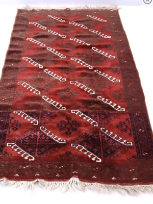 Orientalisk röd matta med mönster - Säljer en orientalisk matta i rött med geometriska mönster i vitt, svart och mörkblått. Mattan har fransar på kortsidorna och ett klassiskt, handknutet utseende. Perfekt som inredningsdetalj för att skapa en mysig känsla i rummet.